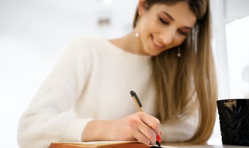 Smiling woman in white sweater writing in notebook